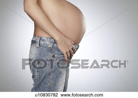 Stock Image - Pregnant woman wearing jeans mid section side view studio shot. Fotosearch