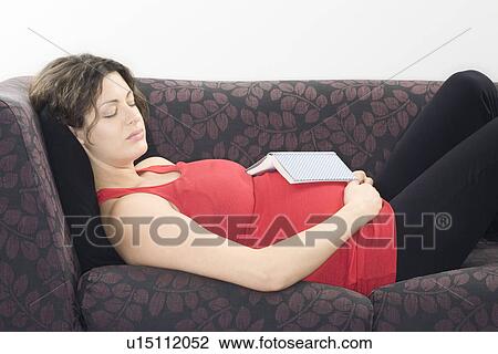 Stock Image - Pregnant woman with book sleeping on sofa. Fotosearch