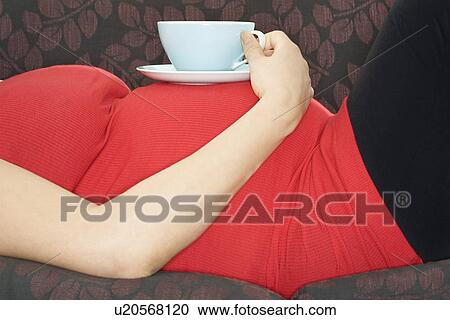 Pregnant woman with drink on sofa mid section View Large Photo Image Stock Image - Pregnant woman with drink on sofa mid section. Fotosearch