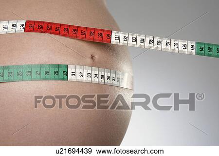 Pregnant woman with tape measure around abdomen mid section close up studio shot View Large Photo Image Stock Photo - Pregnant woman with tape measure around abdomen mid section close up studio shot. Fotosearch