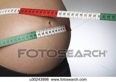 Pregnant woman with tape measure around abdomen mid section close up studio shot View Large Photo Image Stock Photo - Pregnant woman with tape measure around abdomen mid section close up studio shot. Fotosearch