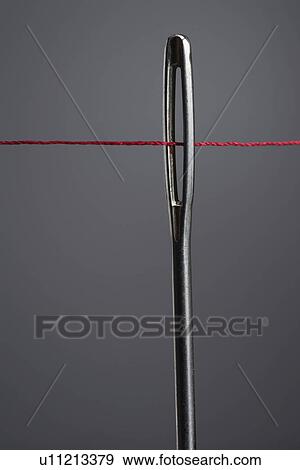 Stock Photo - Red thread going through needle eye close-up. Fotosearch