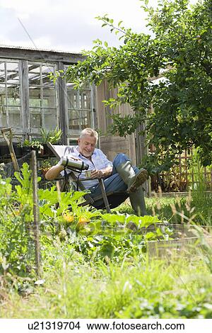 Picture - Senior man pouring drink sitting in garden. Fotosearch