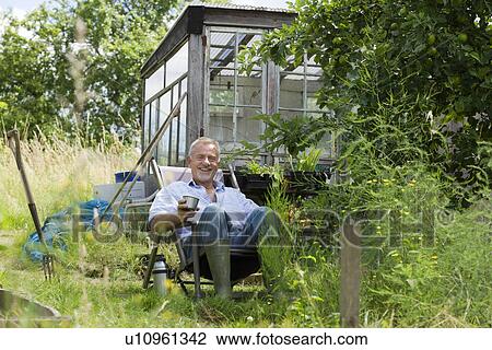 Stock Image - Senior man pouring drink sitting in garden. Fotosearch