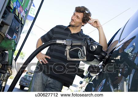 Stock Image - Smiling man refueling car at natural gas station. Fotosearch