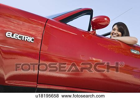 Stock Photo - Smiling woman in red electric car. Fotosearch