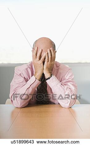 Stock Image - Streessed Businessman Sitting at Meeting Table Head in Hands. Fotosearch