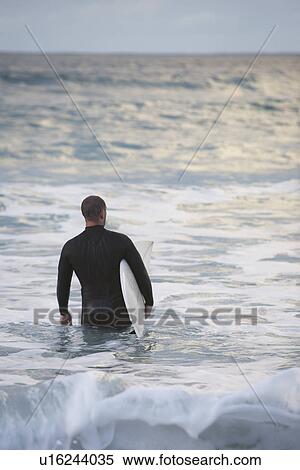 Surfer carrying surfboard into sea back view View Large Photo Image Stock Photography - Surfer carrying surfboard into sea back view. Fotosearch