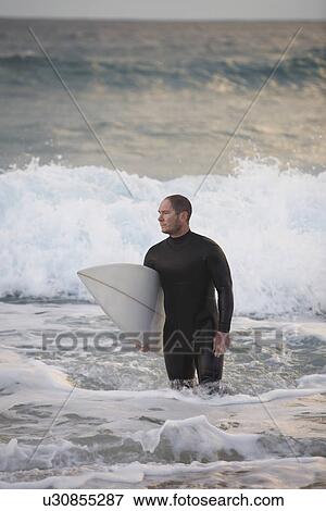 Stock Photo - Surfer carrying surfboard out from sea. Fotosearch
