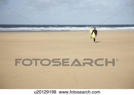 Surfer carrying surfboard walking on beach back view View Large Photo Image Stock Photo - Surfer carrying surfboard walking on beach back view. Fotosearch