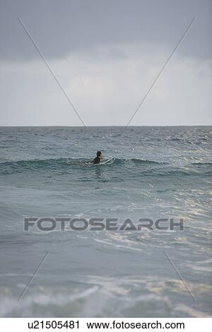 Stock Image - Surfer sitting on surfboard in sea side view. Fotosearch