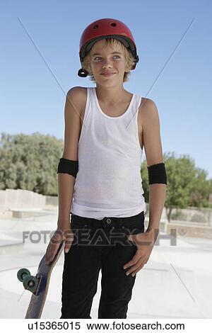 Stock Photography - Teenage boy (13-15) with skateboard at skateboard park portrait. Fotosearch