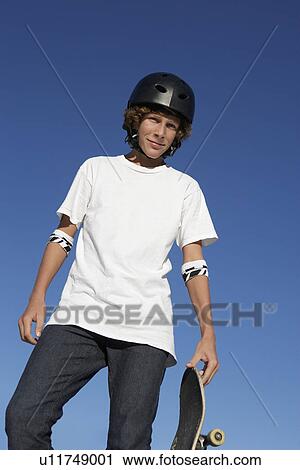 Stock Image - Teenage boy (16-17) holding skateboard outdoors portrait. Fotosearch