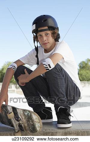 Stock Image - Teenage boy (16-17) with skateboard at skateboard park portrait. Fotosearch