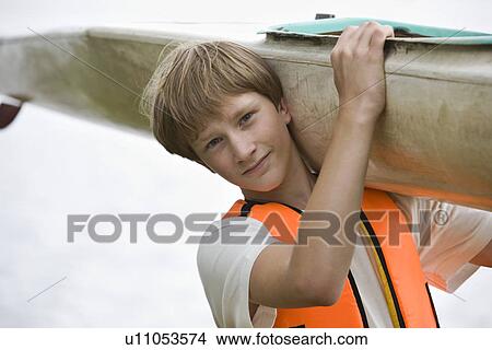 Picture - Teenage boy carrying kayak. Fotosearch