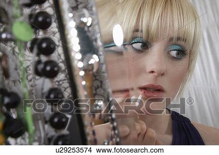 Picture - Teenage girl (16-17) applying lip gloss. Fotosearch