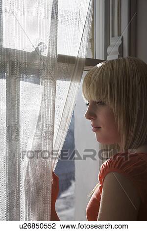 Stock Image - Teenage girl (16-17) looking through window. Fotosearch
