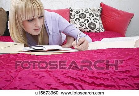 Stock Image - Teenage girl (16-17) lying on bed writing. Fotosearch