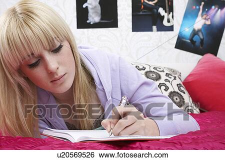 Stock Photograph - Teenage girl (16-17) lying on bed writing diary. Fotosearch