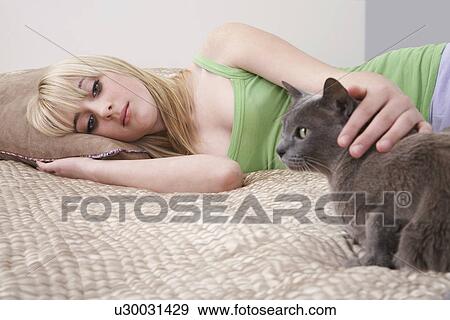 Stock Photo - Teenage girl (16-17) lying on bed with cat. Fotosearch