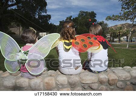 Stock Image - Three girls (7-12) wearing costumes sitting in park. Fotosearch