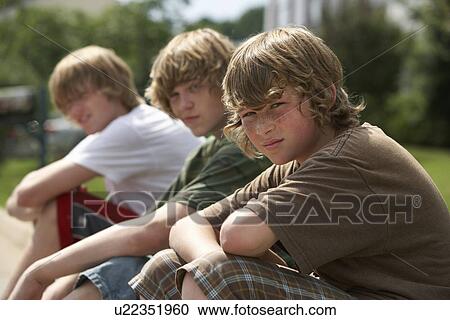 Stock Image - Three teenage brothers (13-17) sitting on street curb portrait. Fotosearch