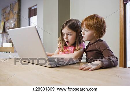 Stock Photo - Two girls (5-6) at table using laptop. Fotosearch
