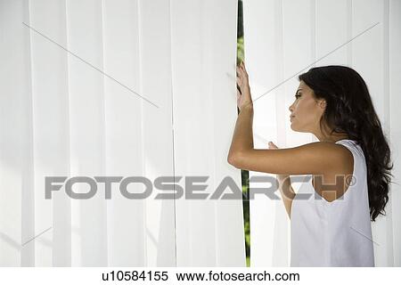 Stock Photography - Woman looking trough curtains. Fotosearch