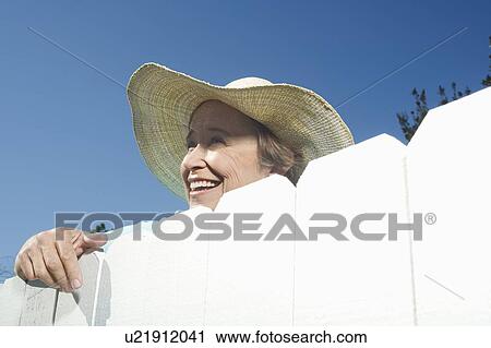 Stock Image - Woman peering over garden fence. Fotosearch
