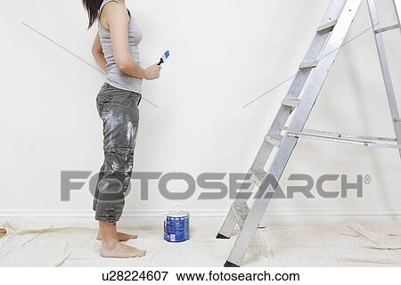 Stock Photo - Woman ready to paint wall low section. Fotosearch