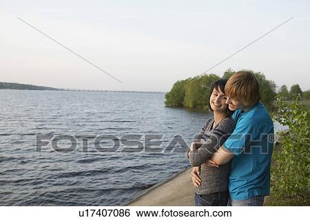 Stock Photograph - Young Couple Cuddling on Lakeshore. Fotosearch