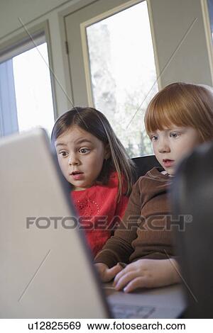 Young girls (5-6) on sofa using laptop surprised View Large Photo Image Stock Photo - Young girls (5-6) on sofa using laptop surprised. Fotosearch