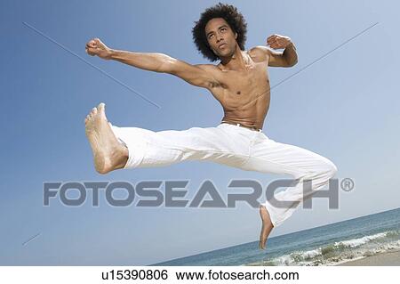 Stock Photograph - Young man exercising on beach. Fotosearch