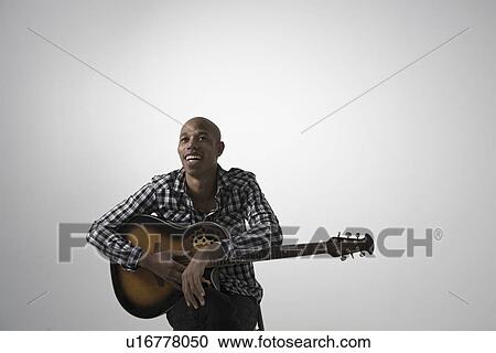 Stock Image - Young man holding guitar smiling. Fotosearch