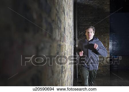 Picture - Young man jogging along side brick wall at night. Fotosearch