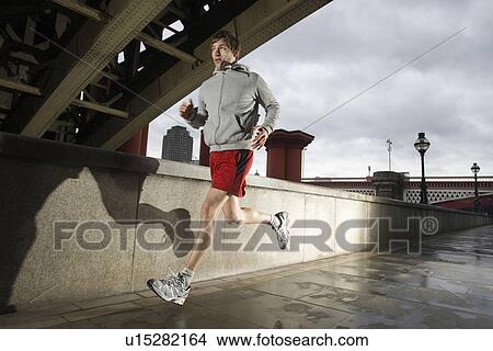 Young man jogging besides the Thames in London on stormy day View Large Photo Image Picture - Young man jogging besides the Thames in London on stormy day. Fotosearch