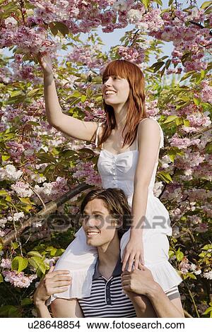 Picture - Young Man Lifting Woman up to Tree Branch. Fotosearch