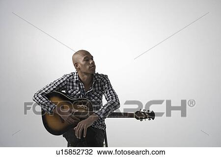 Stock Image - Young pensive man holding guitar. Fotosearch