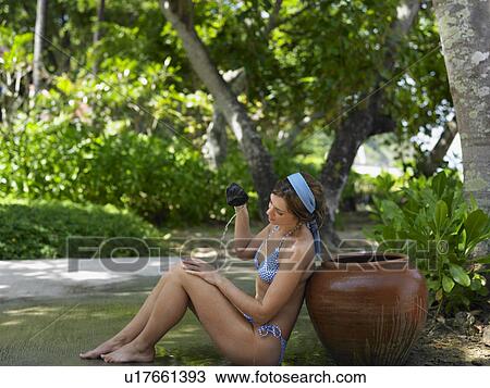 Stock Image - Young Woman in Bikini Pouring Water on Self. Fotosearch