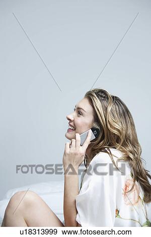 Stock Photo - Young woman in dressing gown using mobile phone in bedroom. Fotosearch