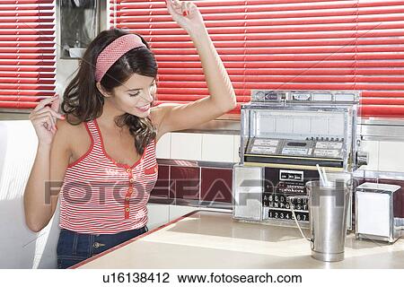 Stock Image - Young Woman Listening to Music in a Diner. Fotosearch
