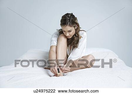 Young woman painting toe nails on bed View Large Photo Image Stock Image - Young woman painting toe nails on bed. Fotosearch