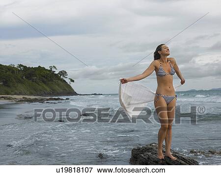 Stock Photo - Young Woman Standing on Rock at Beach. Fotosearch