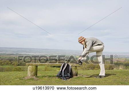 Stock Image - Young Woman Tying Her Shoe on a Park Bench. Fotosearch
