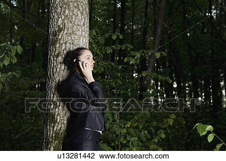 Stock Image - Young woman using mobile phone in forest. Fotosearch