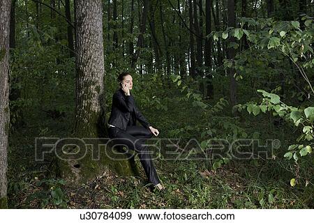 Stock Photo - Young woman using mobile phone in forest. Fotosearch