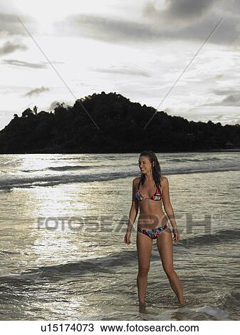 Stock Image - Young Woman Wading in Ocean at Sunset. Fotosearch