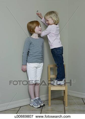 4-5 year old girl measures 7-8 year old against wall View Large Photo Image Stock Photo - 4-5 year old girl measures 7-8 year old against wall. Fotosearch