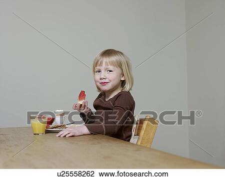 Stock Image - 4-5 year old girl sits eating melon for breakfast. Fotosearch