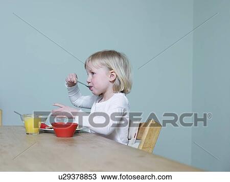 Stock Image - 4-5 year old sits eating breakfast. Fotosearch
